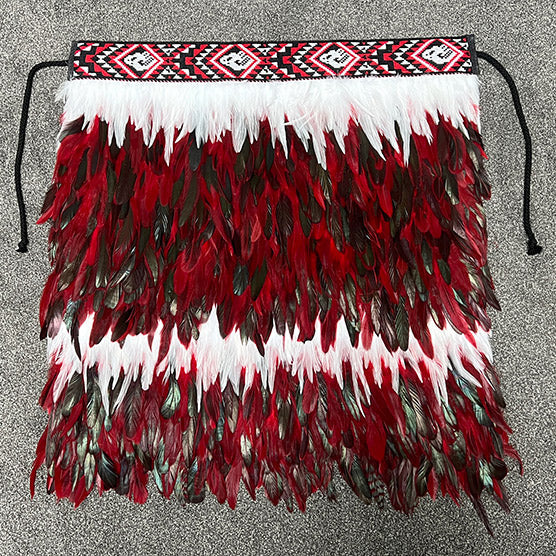 Handmade M?ori Korowai cloak featuring Pohutukawa flowers, vibrant feathers, and traditional taniko trim, symbolizing heritage.