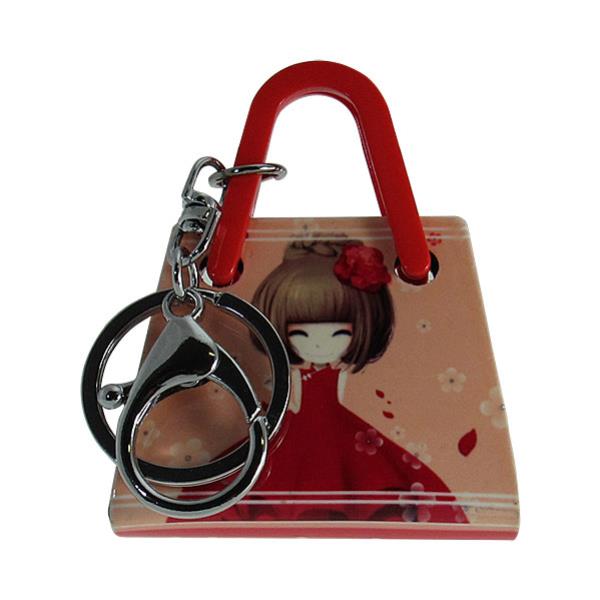 Acrylic 3D keyring shaped like a handbag featuring a girl in a red dress, measuring 5.5cm x 7.0cm.