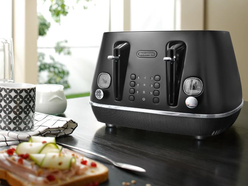 DeLonghi Distinta Moments 4 Slice Toaster in black, featuring dual controls, 6 browning levels, and removable crumb trays.