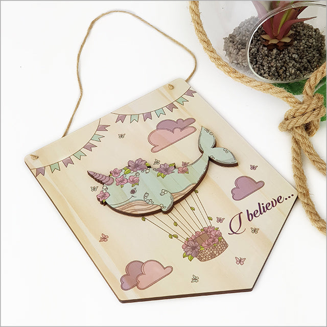 Wall art of a narwhal with 'I Believe' message, crafted from eco-friendly pine veneer, adding whimsy to any decor.