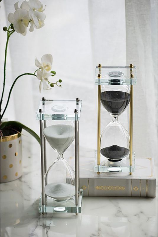 Elegant silver and white hourglass on a clear acrylic and gold stand, perfect for modern decor and conversation starter.