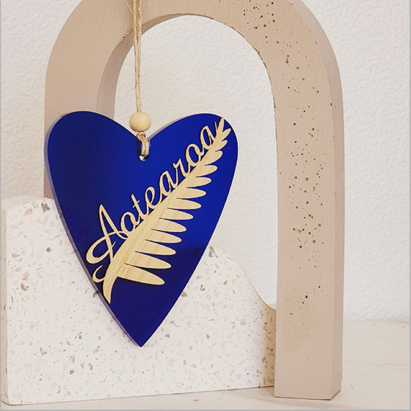 Heart-shaped hanging ornament in blue satin acrylic, featuring a silver fern design, perfect for home decor and gifting.