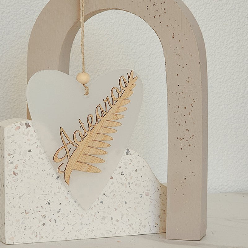 Elegant heart-shaped ornament featuring a laser-cut silver fern, crafted from white satin acrylic, perfect for home decor.