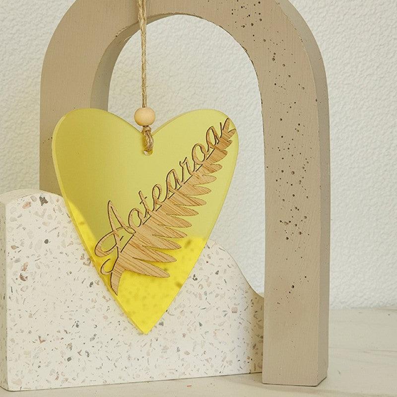 Heart-shaped yellow satin acrylic ornament featuring a laser-cut silver fern design, perfect for home decor or gifting.