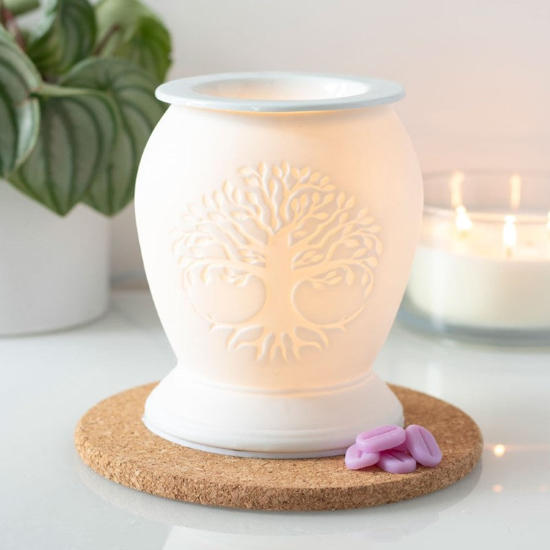 White ceramic electric oil burner with Tree of Life design, casting a warm glow for aromatherapy and cozy ambiance.