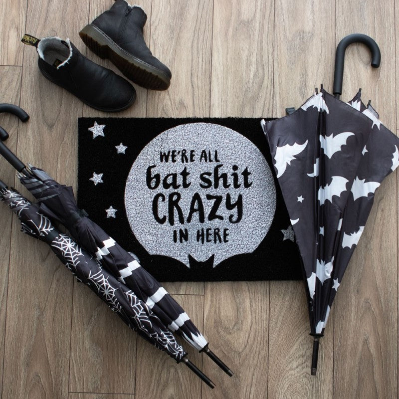 Humorous black doormat with "We're all bat shit crazy" text and full moon design for gothic-inspired decor.