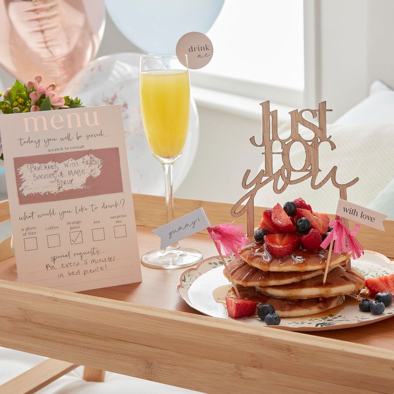 Customisable breakfast in bed set featuring a scratch-to-reveal menu, drink topper, cake topper, and vibrant balloons.