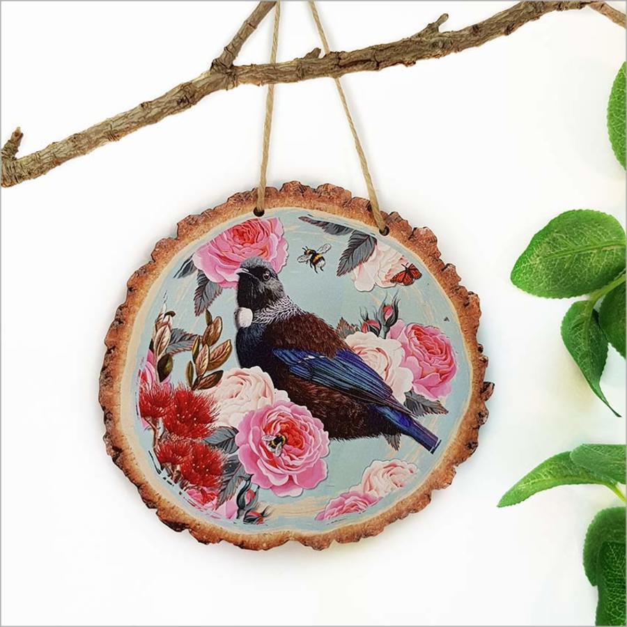 Wood slice wall art featuring a vibrant Tui bird among floral elements, ready to hang and enhancing natural decor.