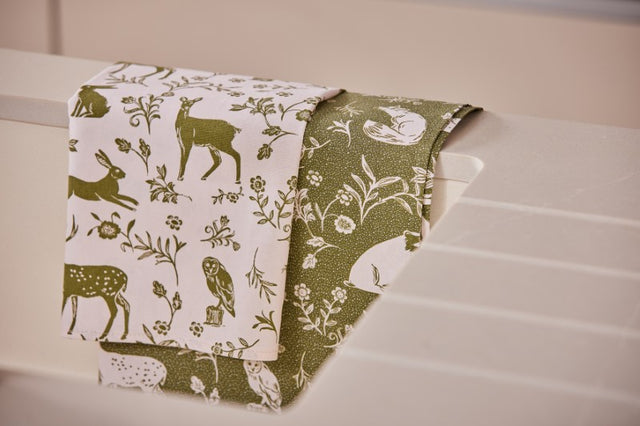 Sage green cotton tea towels featuring woodland creatures and a pollen spot pattern, ideal for eco-friendly kitchen decor.