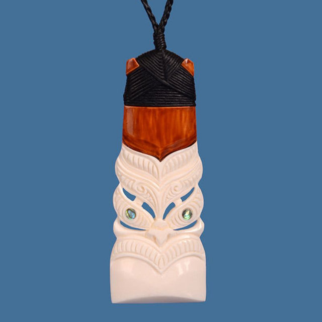 Hand-carved bone pendant featuring a Tiki face with paua shell eyes, symbolizing Maori culture and ancestral protection.