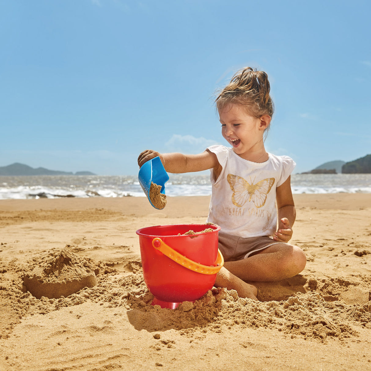 Colorful Hape Scoop & Pail set for toddlers, perfect for beach fun and enhancing fine motor skills while playing with sand and water.