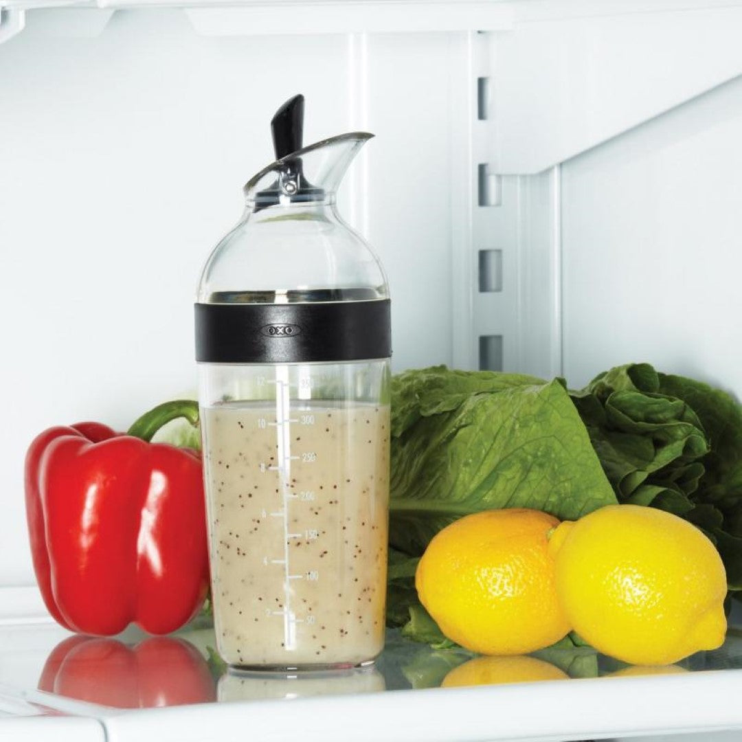 Salad dressing shaker with measurement markings, airtight seal, and one-handed pour lever for easy mixing and serving.