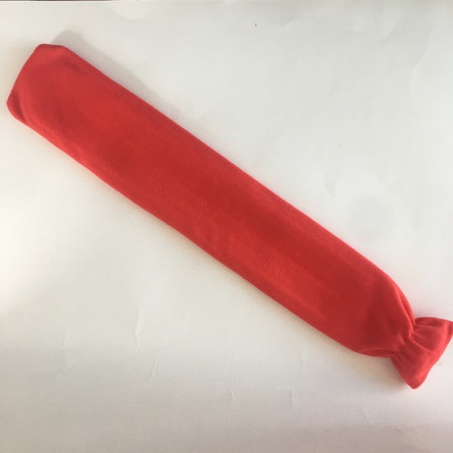 Long red hot water bottle with soft fleece cover for comfort, ideal for soothing aches and keeping warm during chilly nights.