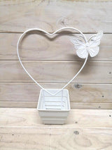Heart-shaped metal garden stake with a butterfly design, providing support and aesthetic charm for plants.