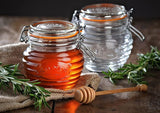 Elegant glass honey pot with embossed beehive design, airtight seal, and beechwood dipper for serving and preserving.