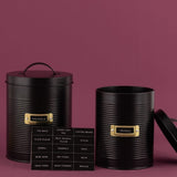 Black storage canister set featuring a ribbed design, gold window frame, and eco-friendly steel; includes two sizes and labels.