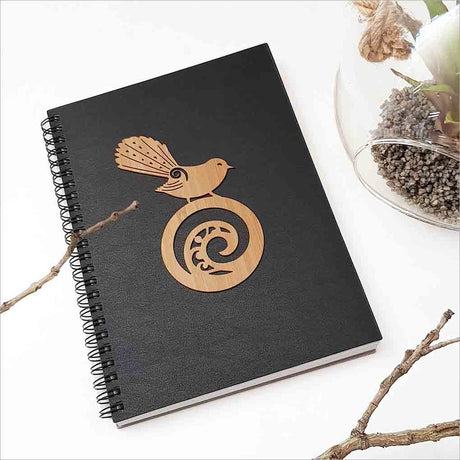 A5 black journal featuring a New Zealand fantail on a koru, perfect for jotting down thoughts and creative ideas.