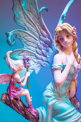 Elegant 31cm fairy figurine with blonde hair, relaxing on a tree branch, accompanied by a pixie and vibrant flowers.