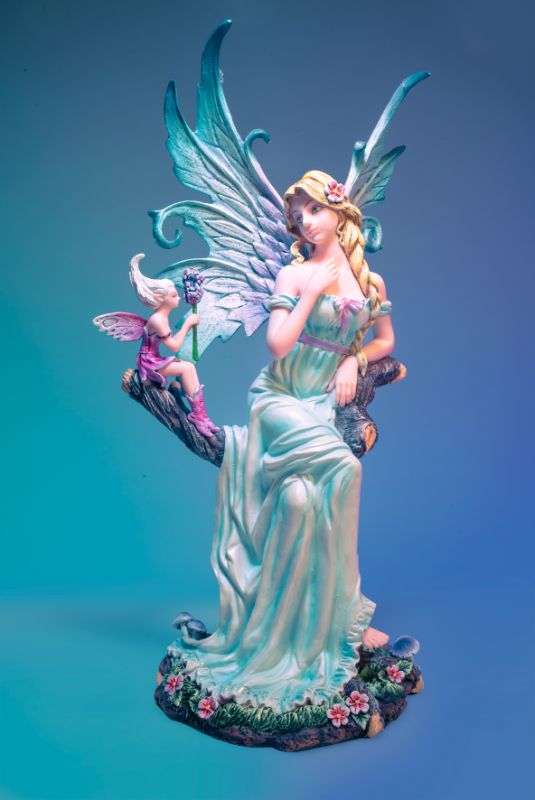 Elegant blonde fairy on a tree branch with a tiny pixie and vibrant flowers, adorned in a pale blue dress and glittery wings.