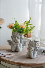 Small cherub angel planter in off-white cement, featuring sculpted wings and a rounded face, ideal for displaying plants.