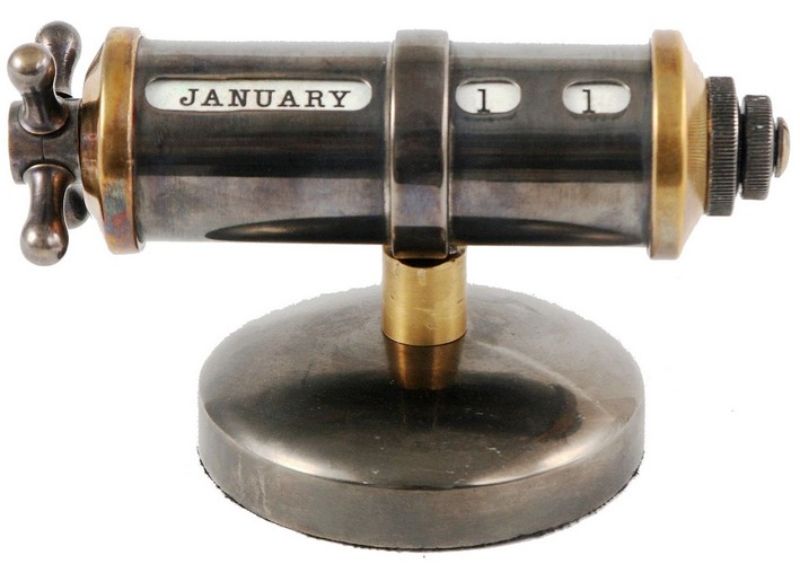 Sleek industrial-style table calendar in brass and nickel, featuring a handle for easy date navigation. Perfect for modern workspaces.