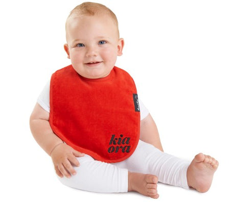 Kiwiana Wonder Bib in vibrant red with 'Kia Ora' design, made of cotton, super-absorbent, and water-resistant for babies.