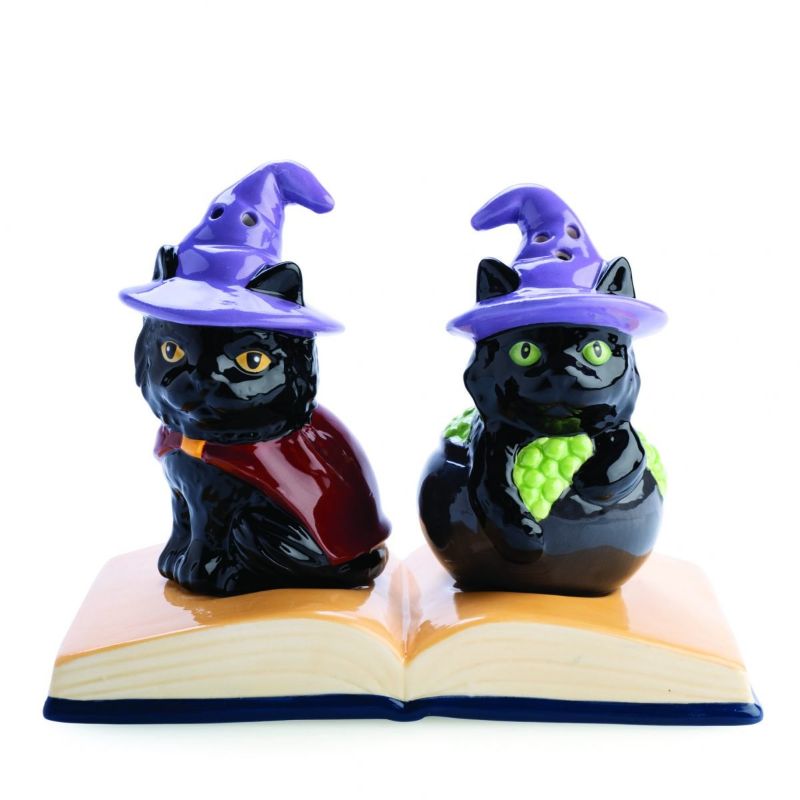 Whimsical salt and pepper shakers shaped like black cats in witches hats, displayed on a vintage book tray.