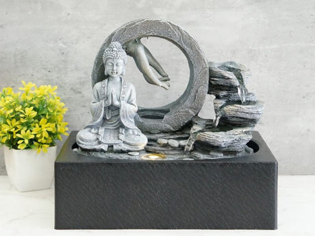 Indoor water fountain featuring Buddha meditating hands, illuminated with warm white light for a serene ambiance.