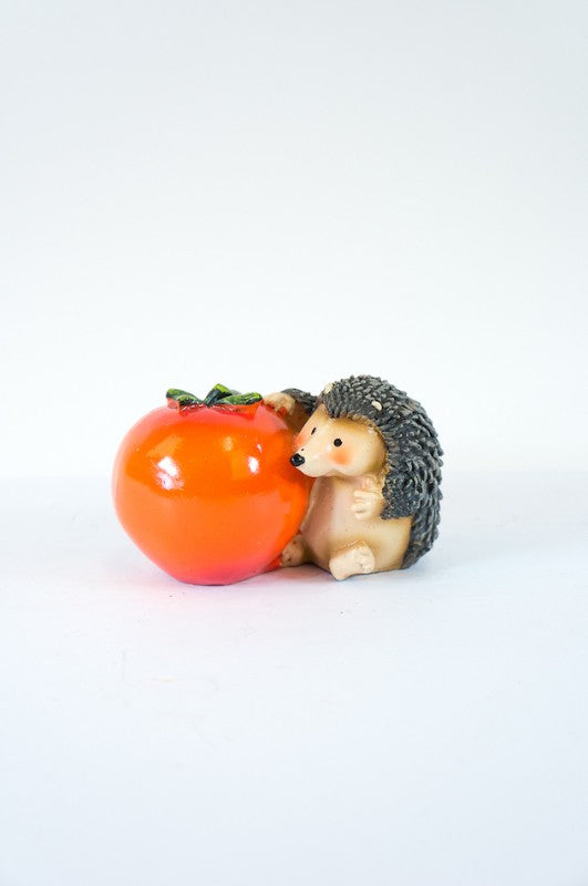 Adorable mini hedgehog garden ornament resting next to a bright tomato, perfect for adding charm to any outdoor space.