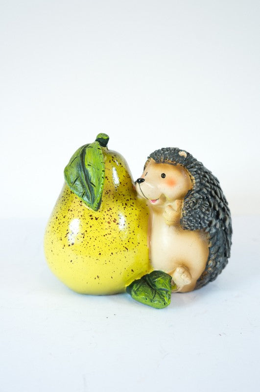 Mini hedgehog garden ornament nuzzling a pear, adding whimsy and charm to outdoor spaces.