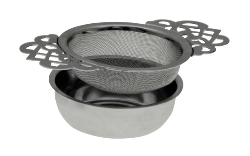 Elegant stainless steel tea strainer with lace handles and drip tray, perfect for brewing loose leaf teas in style.