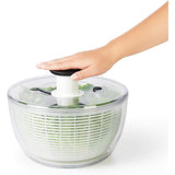 Modern salad spinner with pump mechanism, one-handed operation, clear bowl, non-slip base, and dishwasher-safe parts.