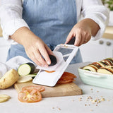 Lightweight hand-held mandoline slicer with soft-grip handle, adjustable thickness, and safety guard for easy, precise slicing.