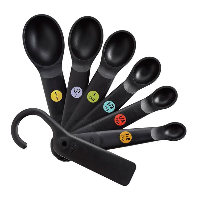 Set of OXO Good Grip 7 Plastic Measuring Spoons in black, featuring clear markings, ergonomic grips, and a convenient scraper.