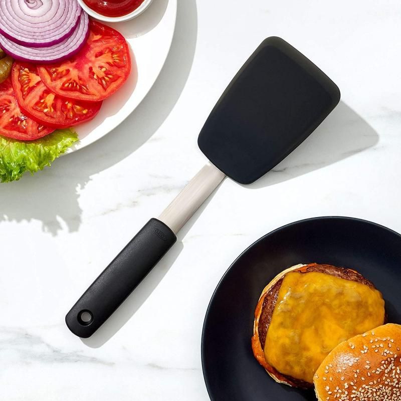 Small silicone flexible turner by OXO with a non-slip grip, ideal for flipping delicate foods in non-stick cookware.