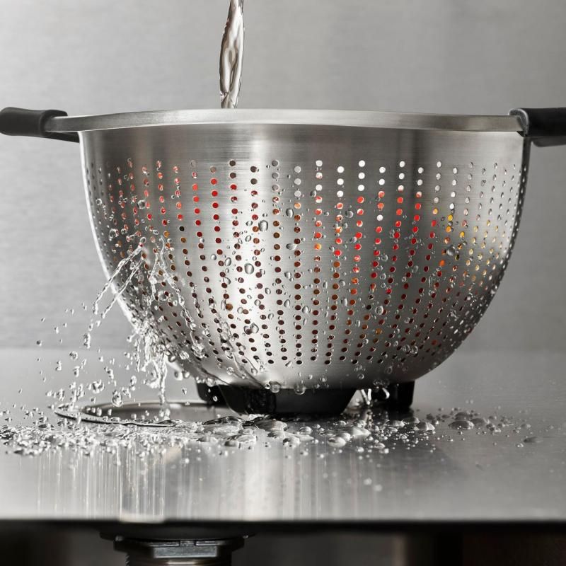 Stainless steel colander with non-slip handles, perfect for rinsing vegetables and straining pasta with stability.