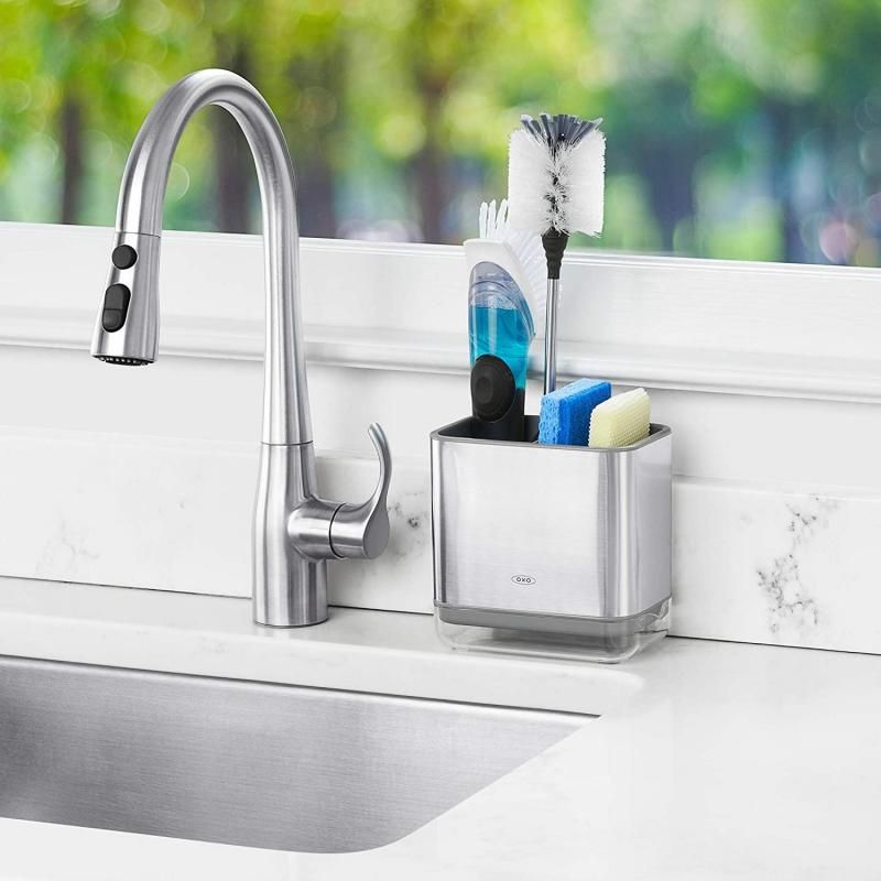 Stainless steel sink caddy with divider for sponges and brushes, featuring ventilation holes and a drain tray for easy cleaning.