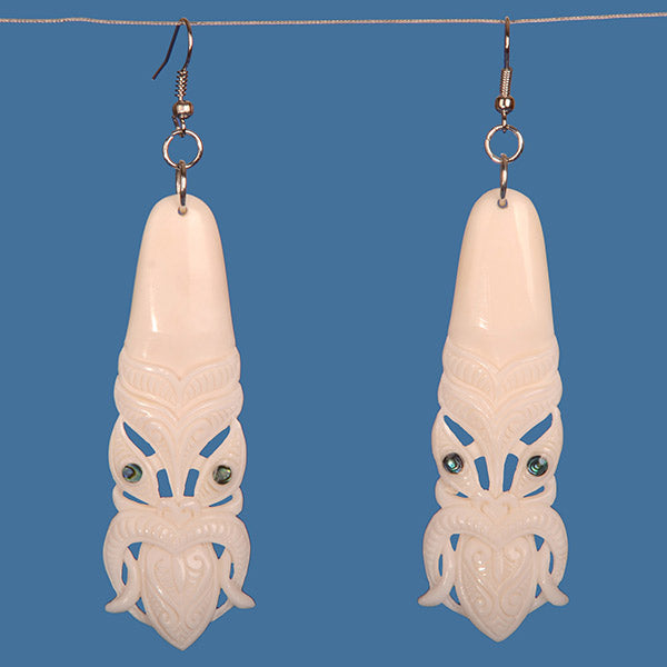 Handcrafted bone earrings featuring intricate Tiki carvings and vibrant paua shell accents, celebrating M?ori artistry and culture.