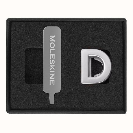 Stylish silver letter pins designed to personalize Moleskine notebooks by attaching to the elastic closure.