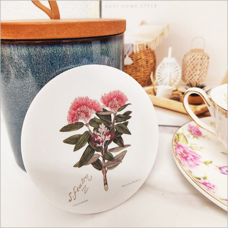 Acrylic coaster featuring vibrant Pohutukawa blossom art by Sarah Featon, 10cm diameter, with a cork base for grip.