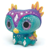 Colorful figurine painting kit featuring two fantasy creatures, acrylic paints, brushes, glitter varnish, and rhinestones for creativity.