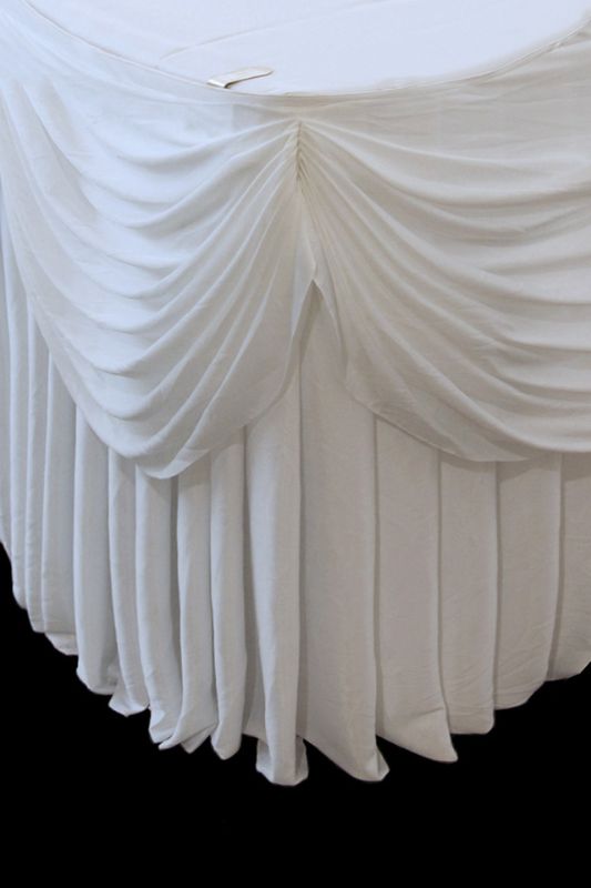 Elegant white round cake table skirt with beautiful swagging, designed for easy attachment and a perfect fit for events.
