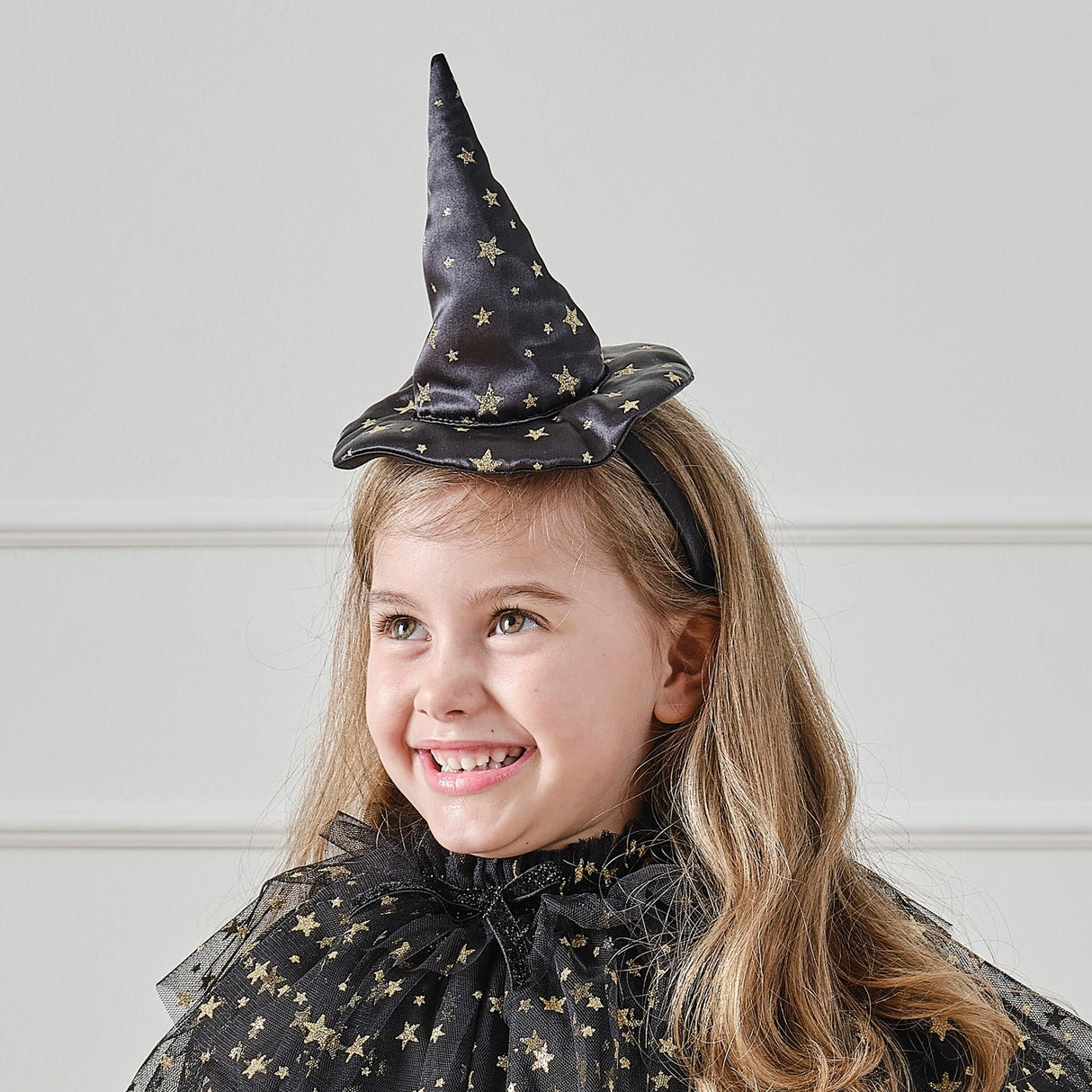 Black satin witch hat headband with shimmering gold stars, perfect for Halloween costumes and imaginative dress-up.