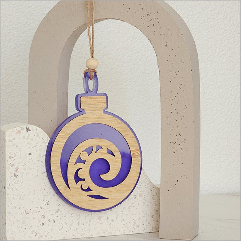 A purple satin acrylic hanging ornament with a unique Koru design, perfect for festive decor and thoughtful gifts.
