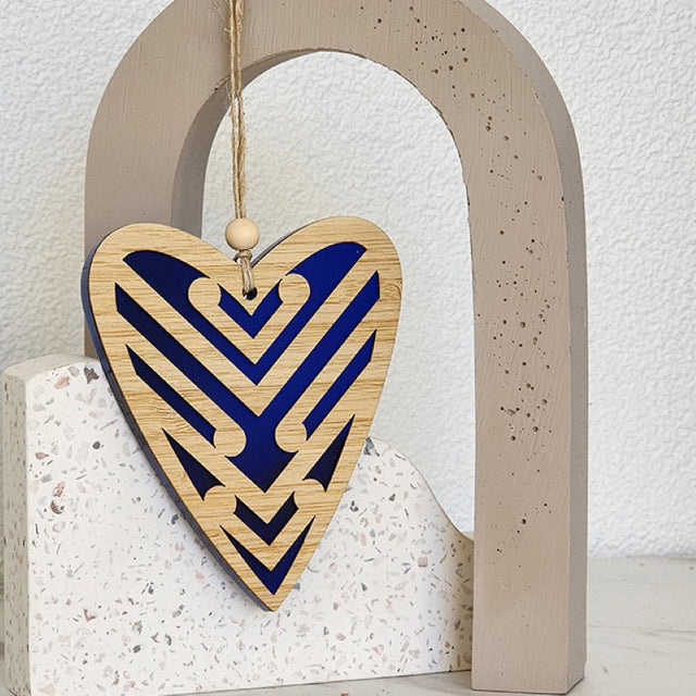 Heart-shaped blue satin acrylic ornament featuring intricate Koru designs, perfect for home decor or gifting.