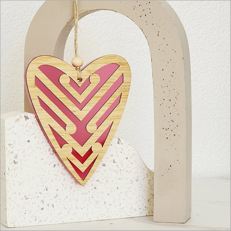 Heart-shaped pink satin acrylic ornament with koru designs, symbolizing growth; perfect for home decor and gifts.