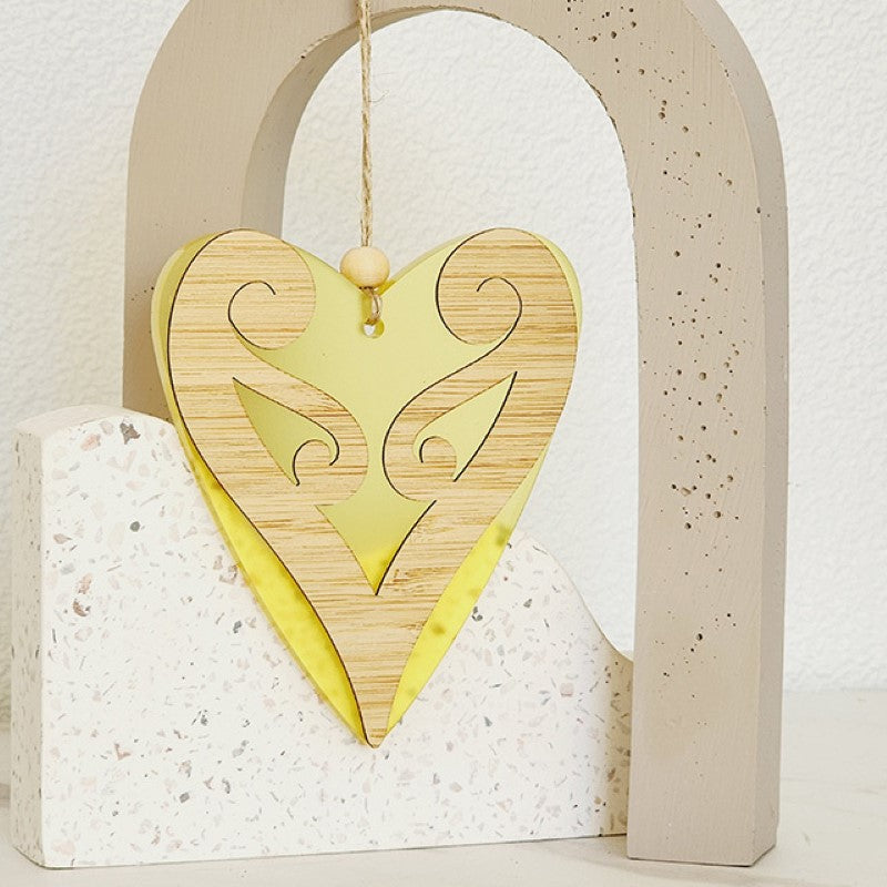 Heart-shaped hanging ornament in yellow satin acrylic, featuring intricate Koru design, perfect for home decor or gifts.