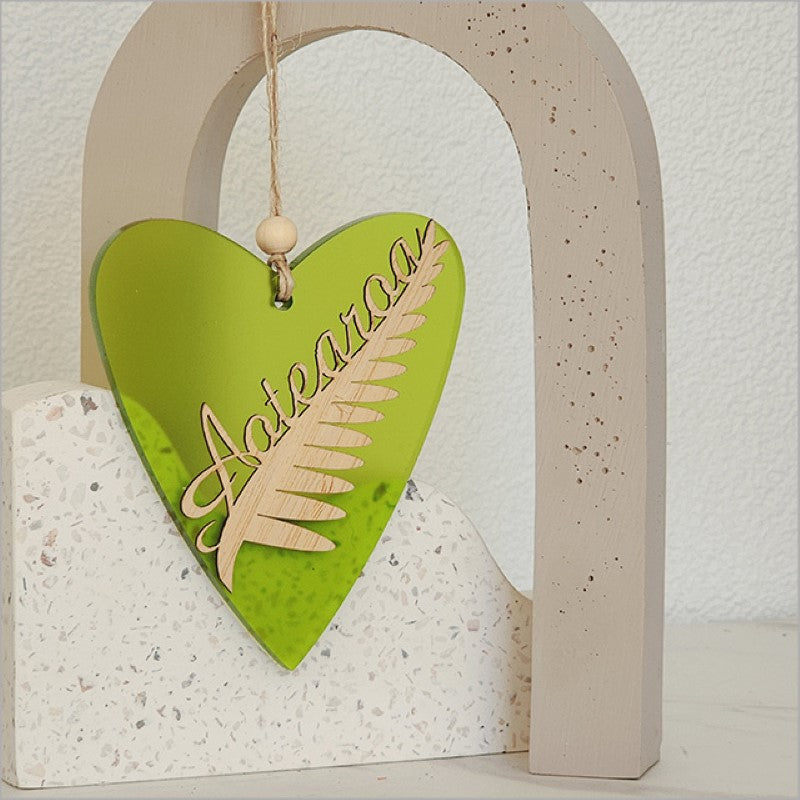Heart-shaped hanging ornament in lime satin acrylic, featuring a silver fern design, perfect for holiday decor and gifting.