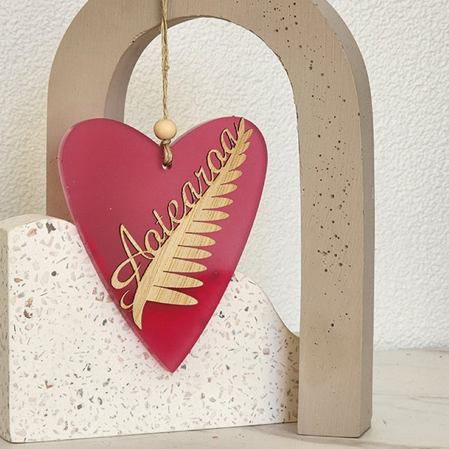 Heart-shaped ornament in pink satin acrylic with a silver fern design, perfect for home decor and gifting.