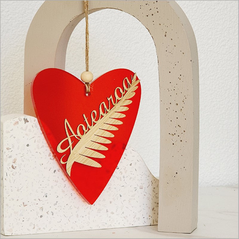 Heart-shaped red satin acrylic ornament featuring a Silver Fern design, perfect for holiday decorating or gifting.